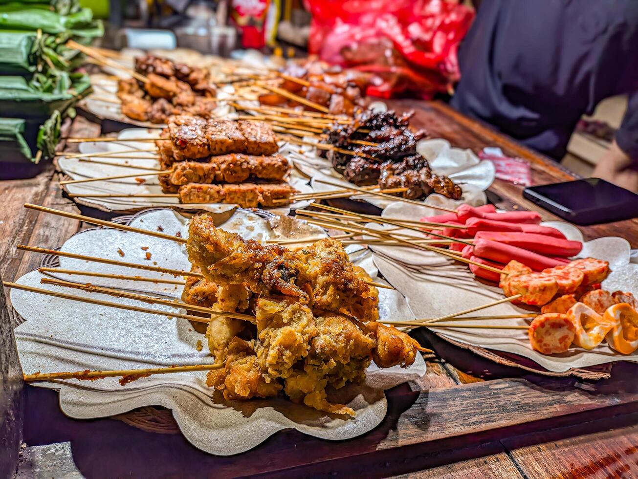 Traditional Indonesian angkringan street food stall with assorted grilled skewers, vibrant night market scene. Perfect for capturing the essence of local cuisine and culture photo