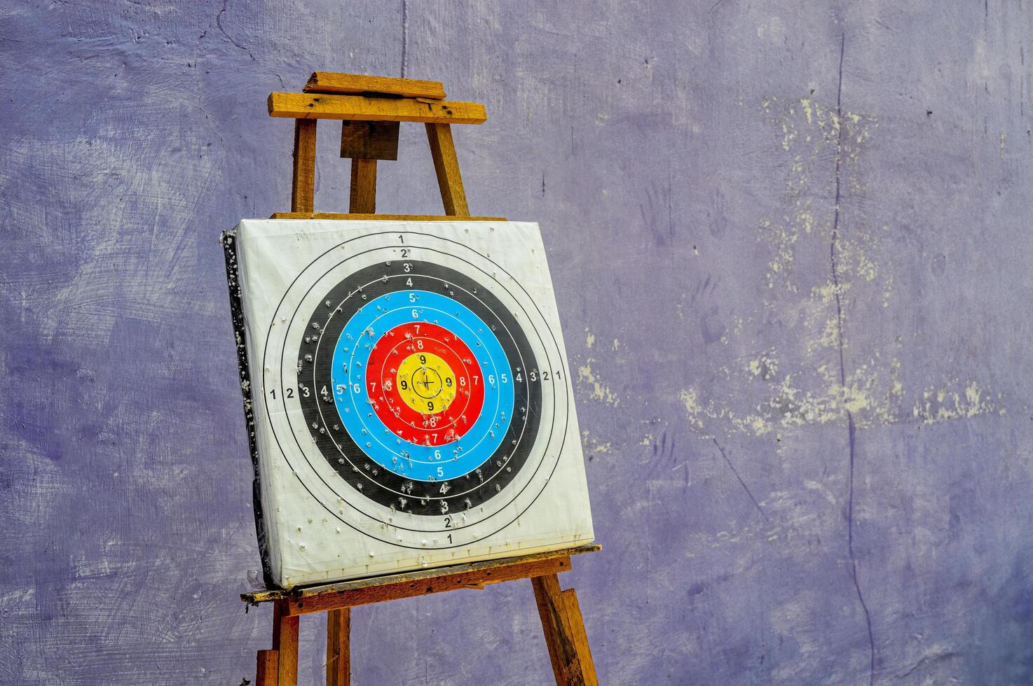 Colorful archery target on wooden easel against textured purple wall, concept of aim, focus and goal achievement. photo