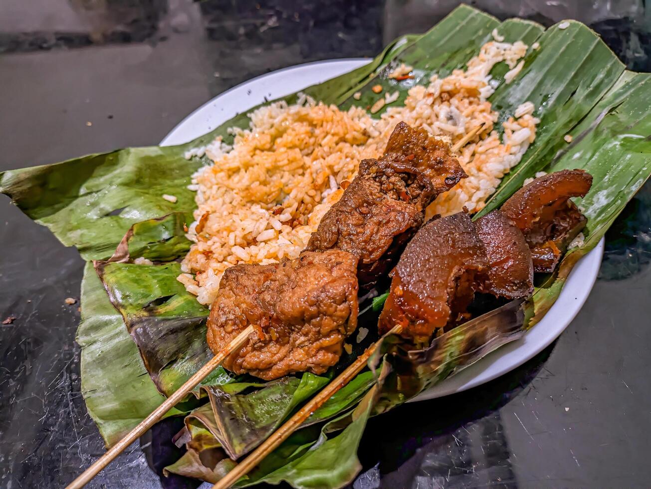 Indonesian grilled rice nasi bakar with cow nose skewers and marinated tofu skewers, served on banana leaves, showcasing traditional street food photo