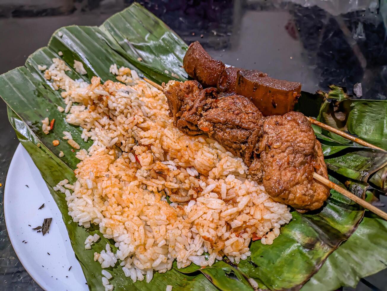 Indonesian grilled rice nasi bakar with cow nose skewers and marinated tofu skewers, served on banana leaves, showcasing traditional street food photo