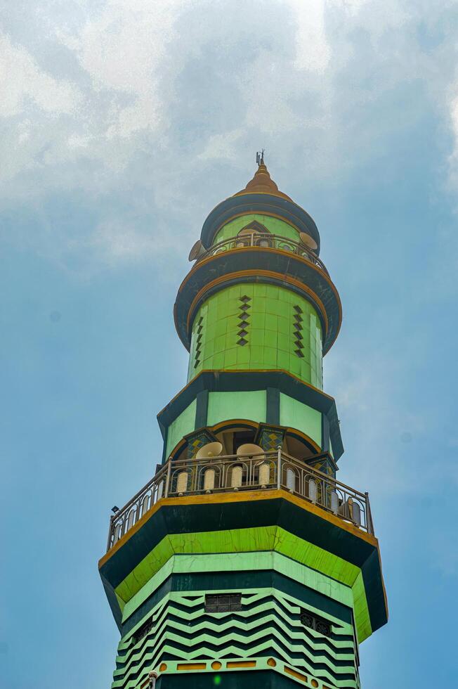Green and gold minaret tower against a clear blue sky with wispy clouds, Islamic architecture, religious symbol photo