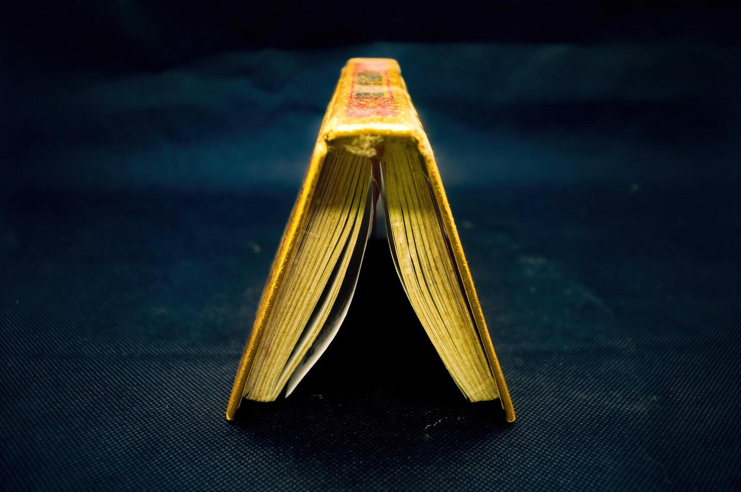 Open Quran book with golden edges on dark background, showcasing intricate Arabic script, symbolizing Islamic faith and spirituality photo