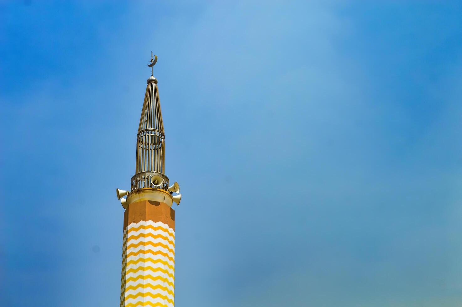 Minaret with yellow and white stripes against a clear blue sky, showcasing Islamic architectural beauty. photo