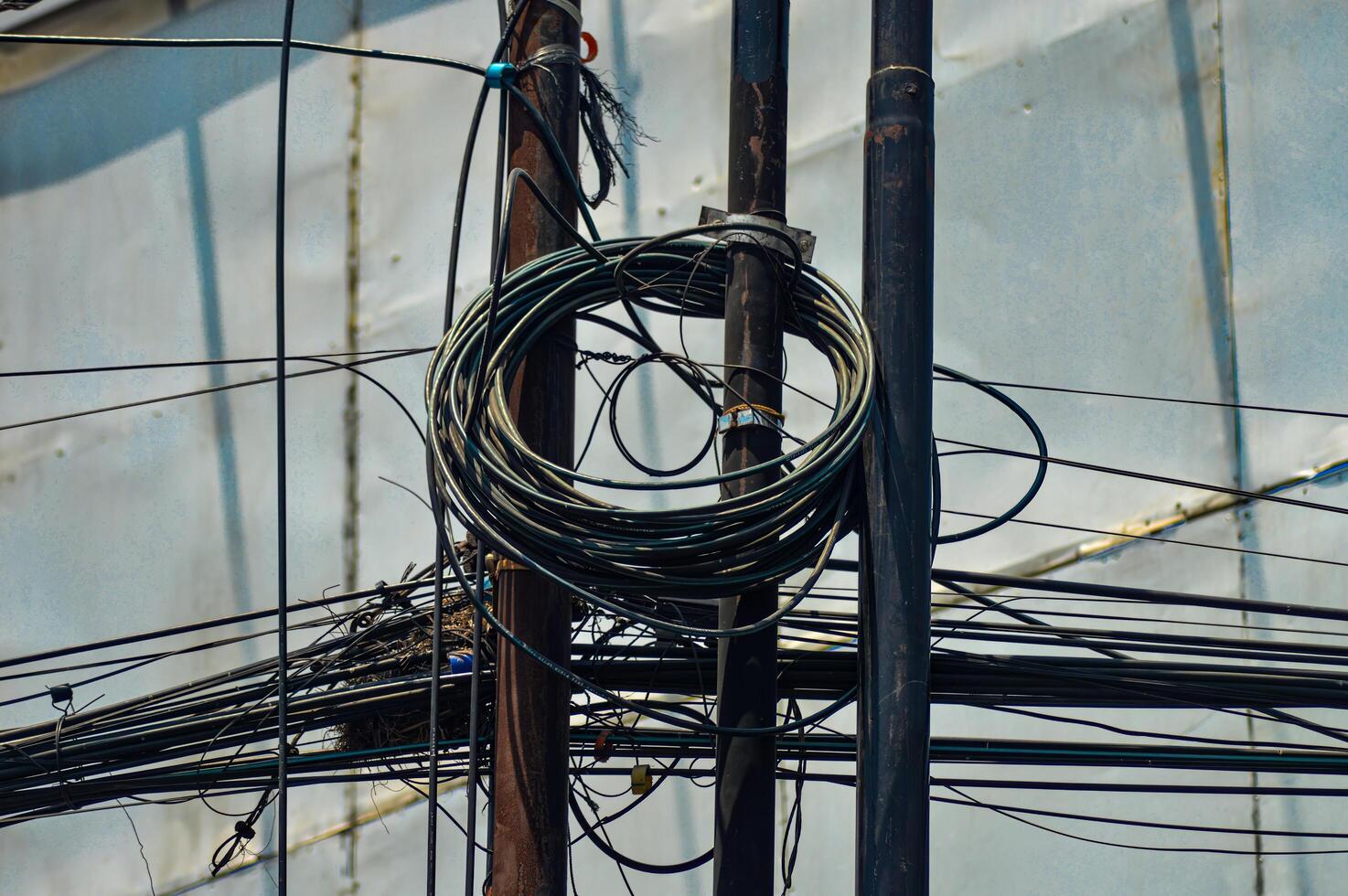 Urban chaos depicted through tangled electrical wires against a building and clear blue sky, showcasing complex city infrastructure photo