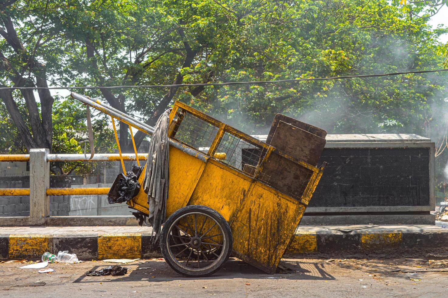 Overturned yellow garbage cart on urban roadside with scattered trash and rising dust, depicting waste management issues photo