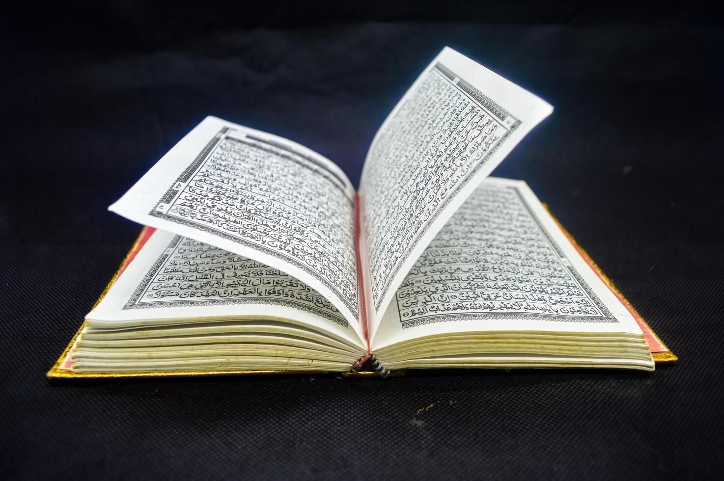 Open Quran book with intricate Arabic script on black background, highlighting the sacred text of Islam. Arabic word translation The Holy Al Quran holy book of Muslim photo
