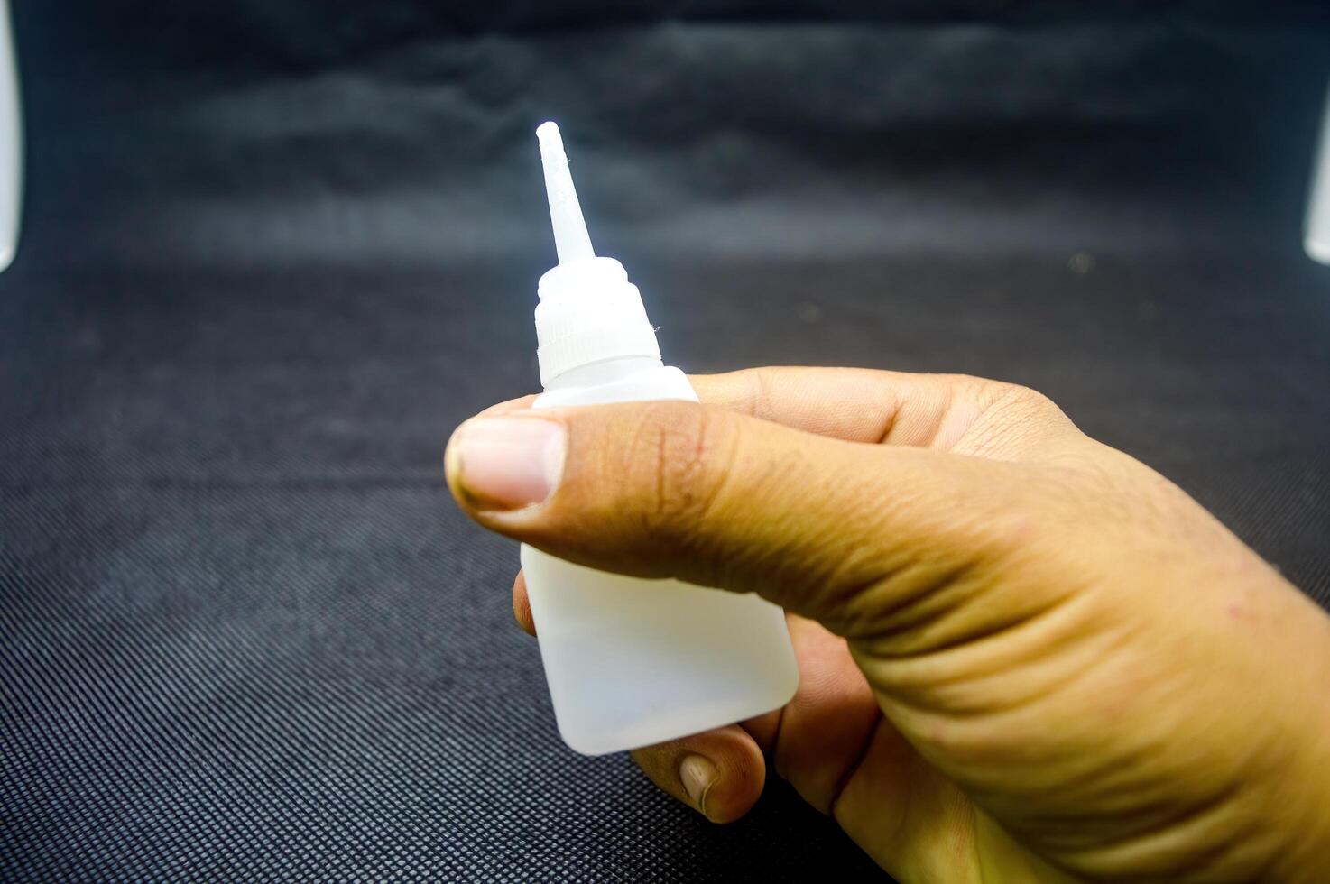 Hand holding a bottle of Cyanoacrylate Ethyl adhesive with a precision applicator tip against a dark background. Ideal for detailed adhesive work in DIY projects, crafts, and repairs photo