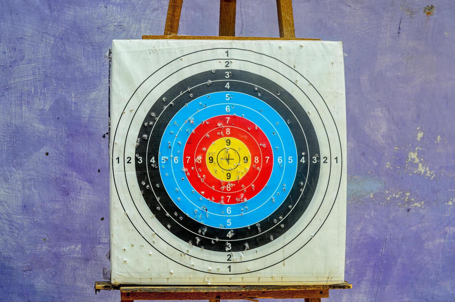 Colorful archery target on wooden easel against textured purple wall, concept of aim, focus and goal achievement. photo
