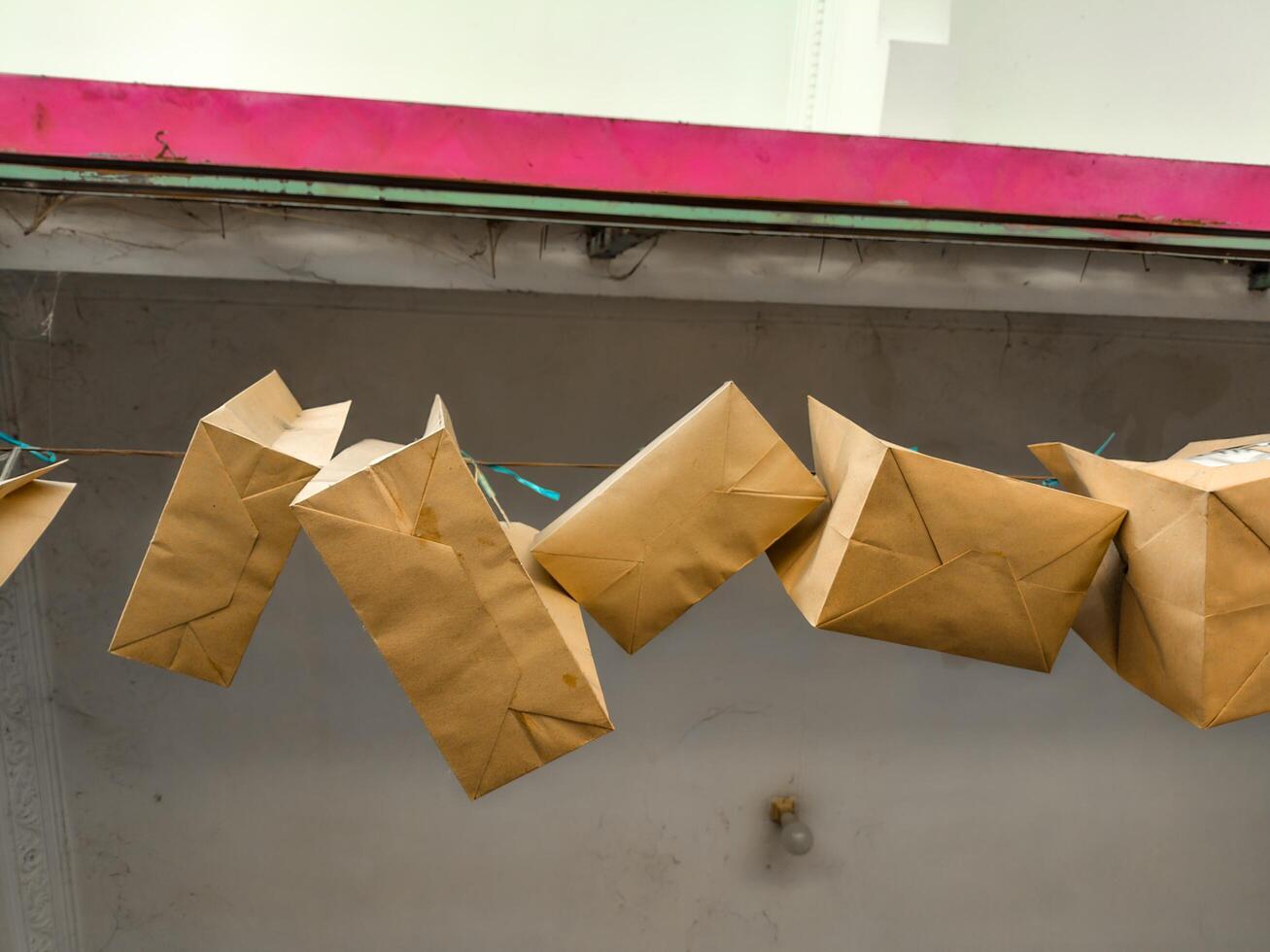 Eco friendly brown paper tote bags hanging on a string against a grey wall with a pink border. Perfect for retail, gift packaging, and promoting sustainable shopping habits photo