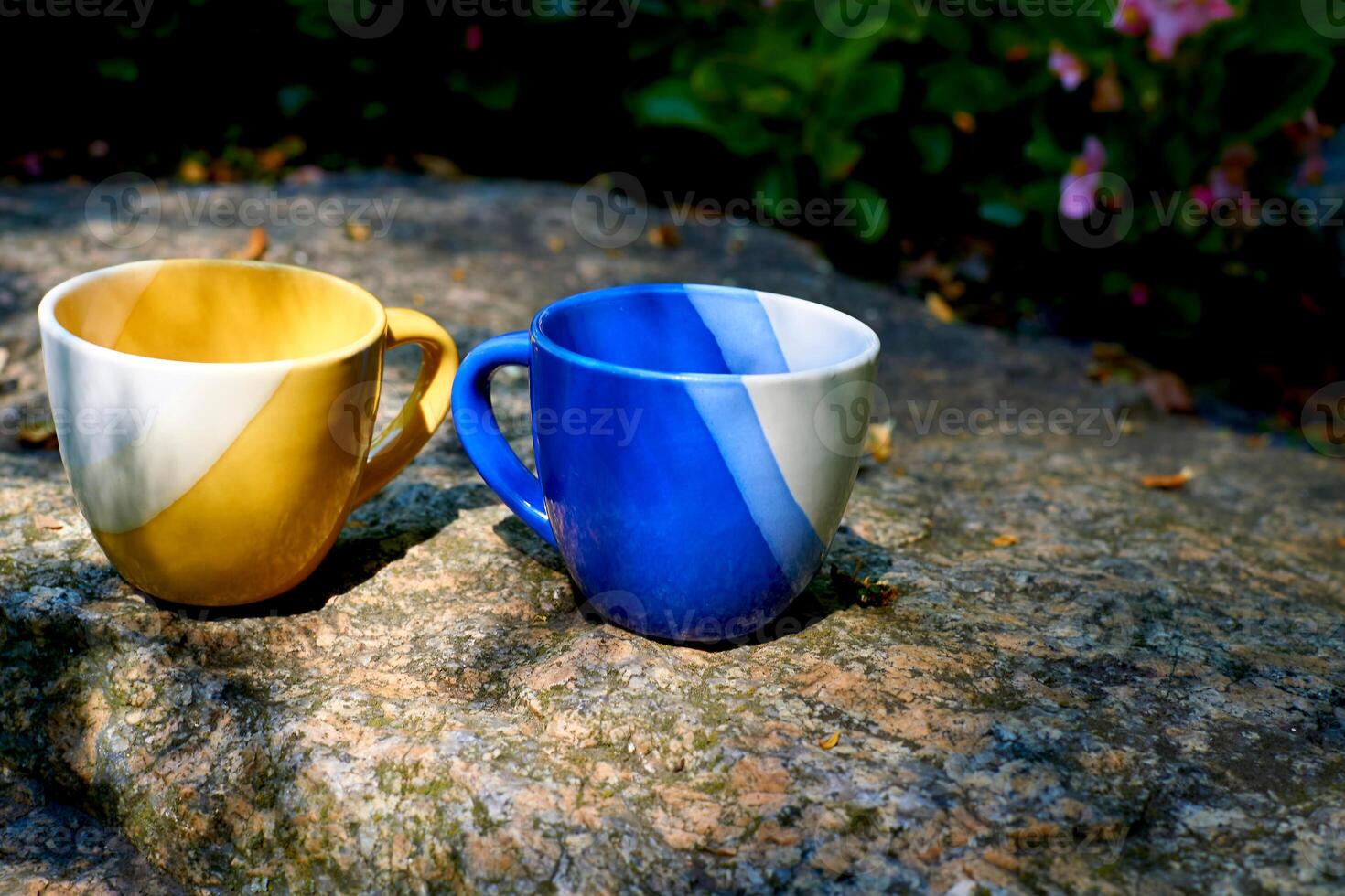 Coffee break,tea time.Yellow blue cups on stone in flower garden photo