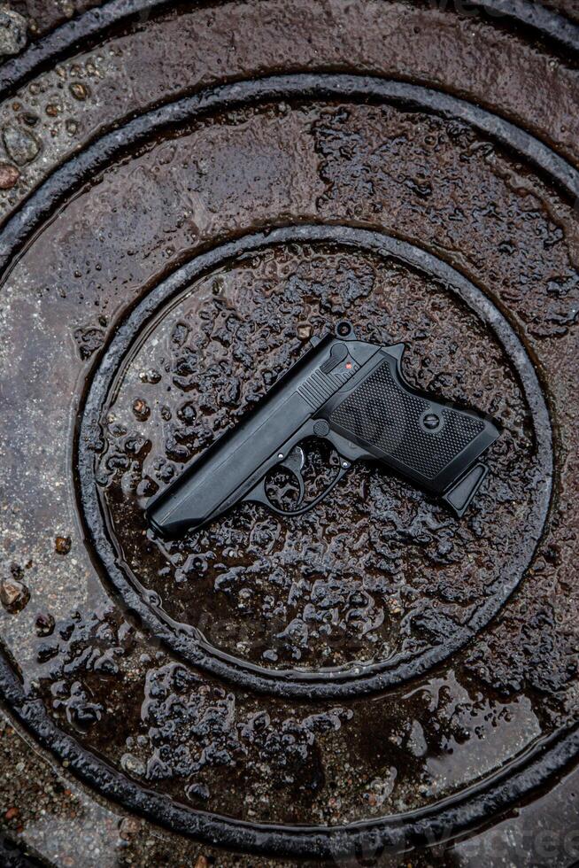 lack handgun on a wet, textured surface, emphasizing contrast between the matte finish of the firearm and the glistening puddles. Ideal for safety, tactical, or firearm-themed content. photo