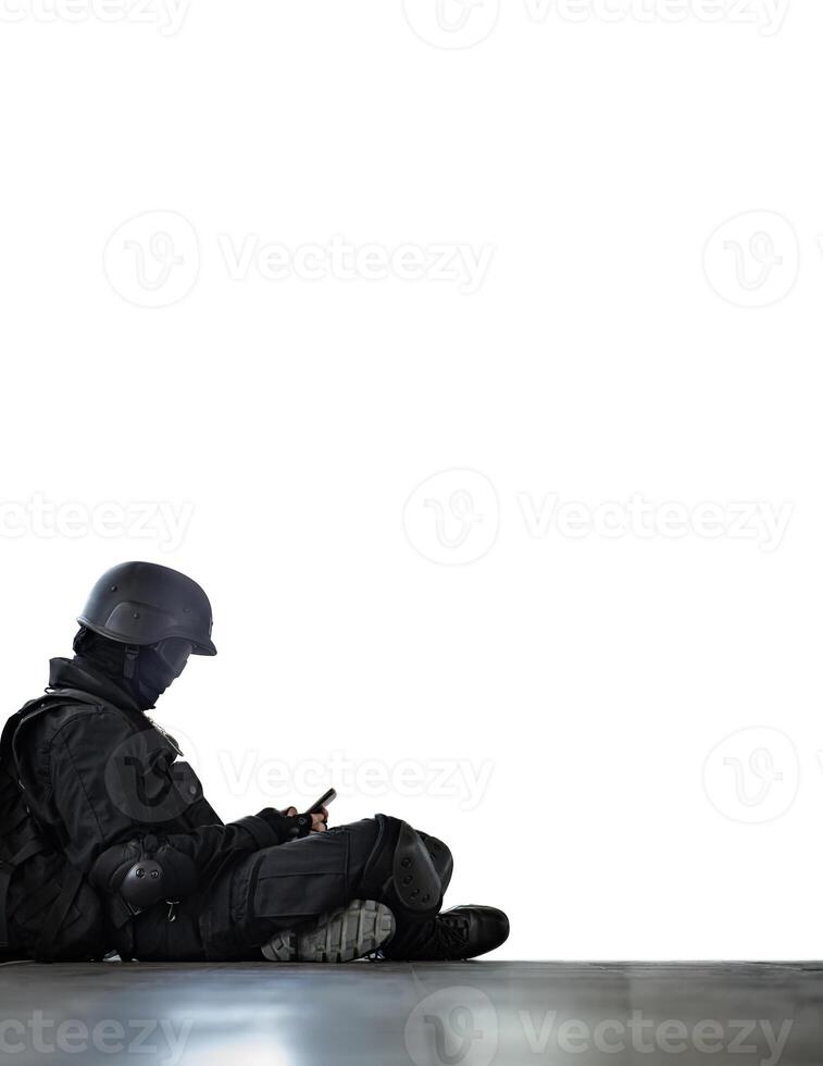 Person in full tactical gear sitting on the ground, engaged with a smartphone, blending modern technology with military attire photo