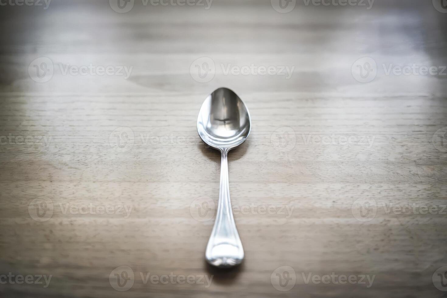Single silver spoon on a wooden table, reflecting natural light. photo