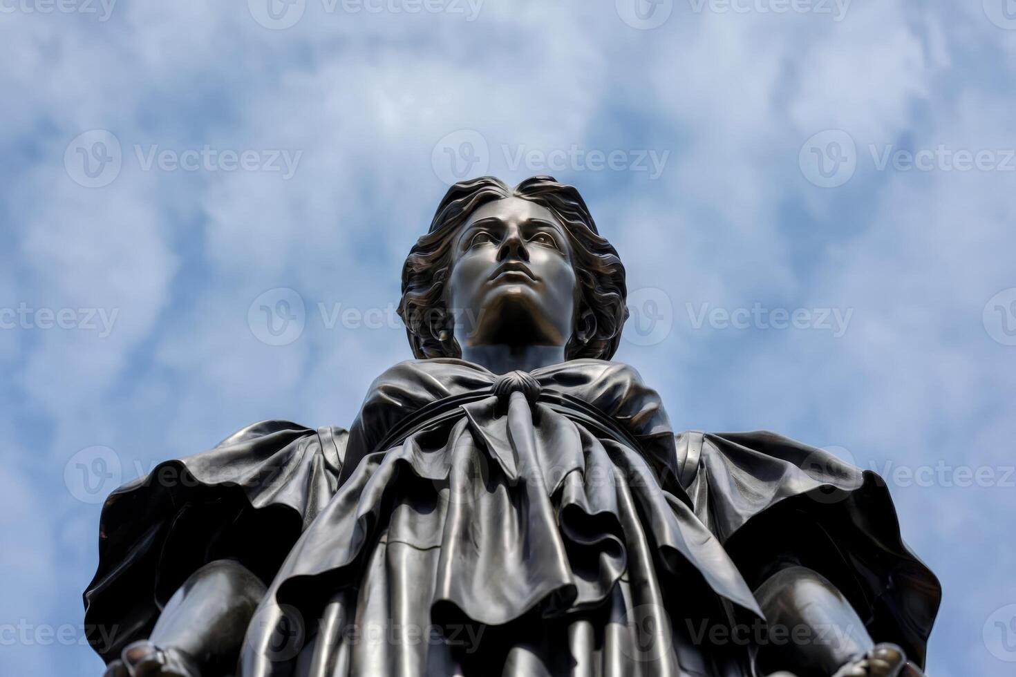 Low-angle view of a statue of a woman against a partly cloudy sky. photo