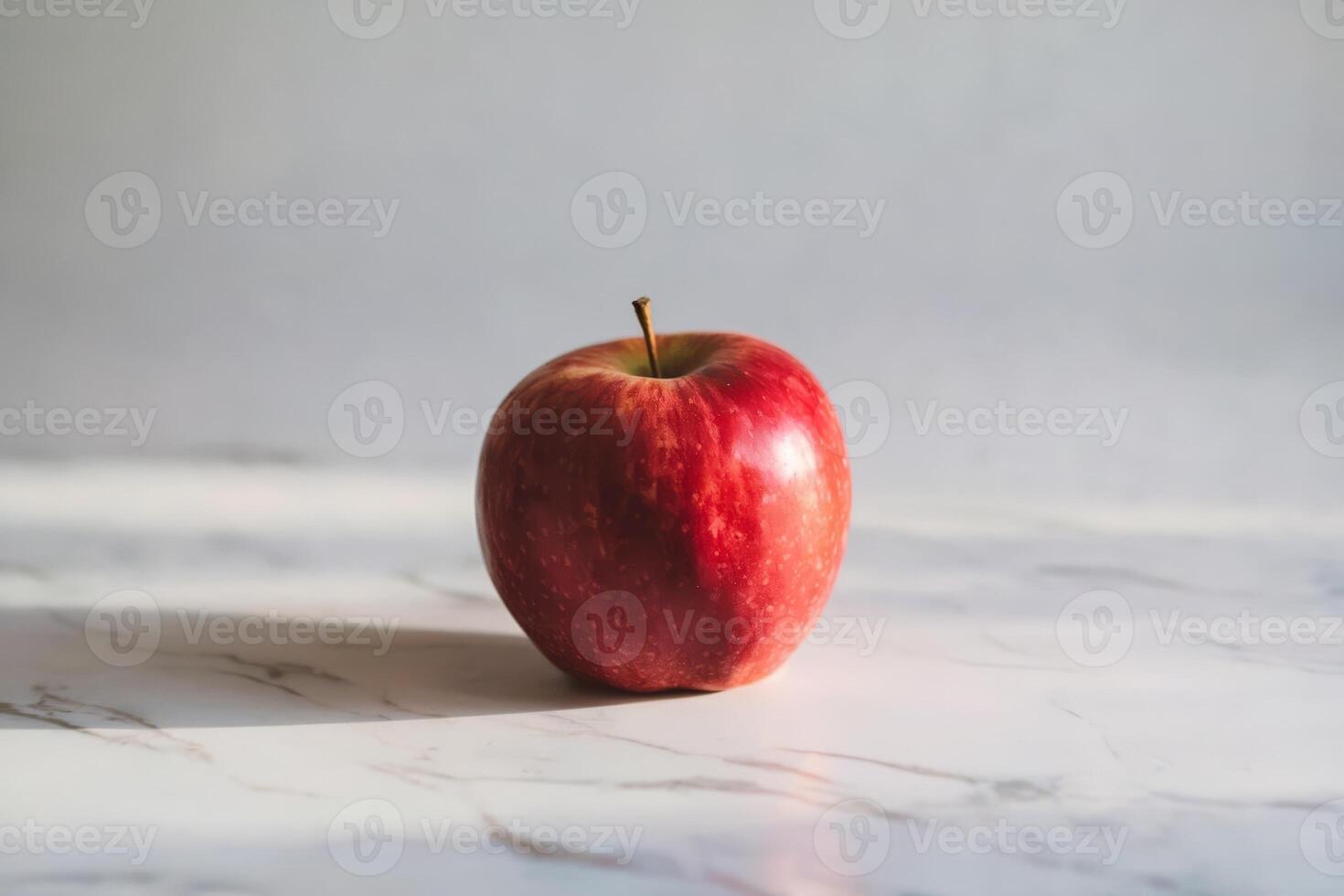 A fresh red apple sits on a marble surface, bathed in natural light. photo
