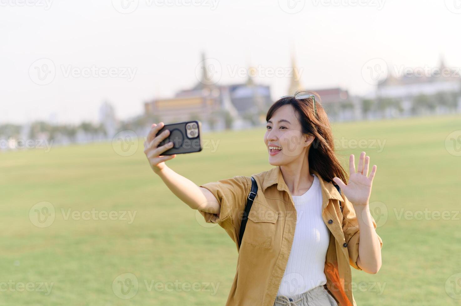 Traveler asian woman in her 30s making a livestream or selfie on smartphone while explores Wat Phra Kaew emerald Buddha. Share the wonders of Thai heritage through her journey. photo