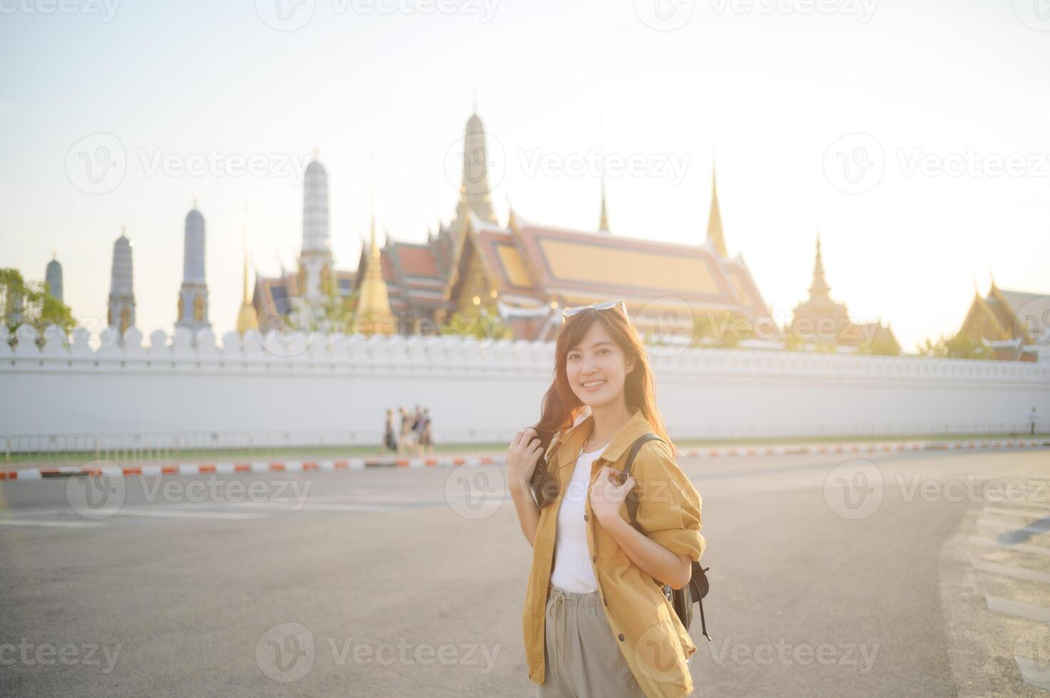 Traveler asian woman in her 30s, backpack slung over her shoulder, explores the intricate details of Wat Pra Kaew with childlike wonder. Sunlight dances on the golden rooftops. photo