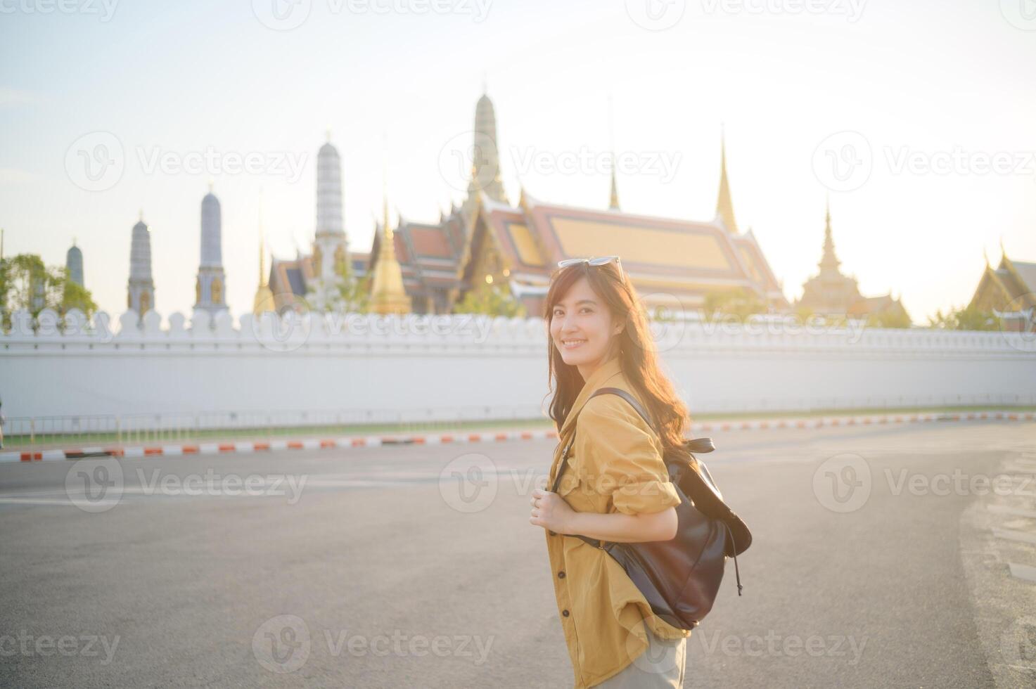 Traveler asian woman in her 30s, backpack slung over her shoulder, explores the intricate details of Wat Pra Kaew with childlike wonder. Sunlight dances on the golden rooftops. photo