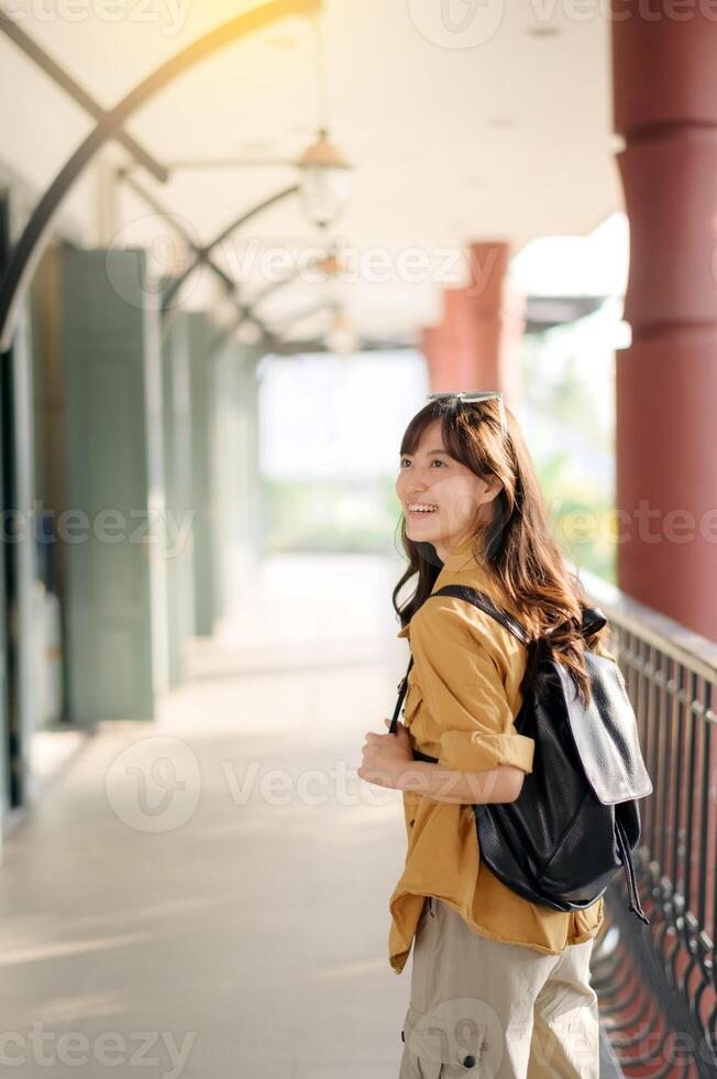 smiling Asian woman in her 30s embarks on a solo journey of exploration. Backpack on, camera ready, she captures the essence of urban adventure. photo