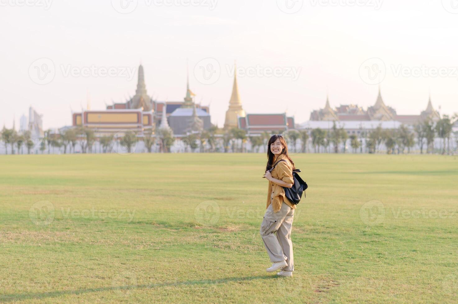 Traveler asian woman in her 30s, backpack slung over her shoulder, explores Wat Pra Kaew with childlike wonder. Sunlight dances on the golden rooftops, and a carefree smile photo