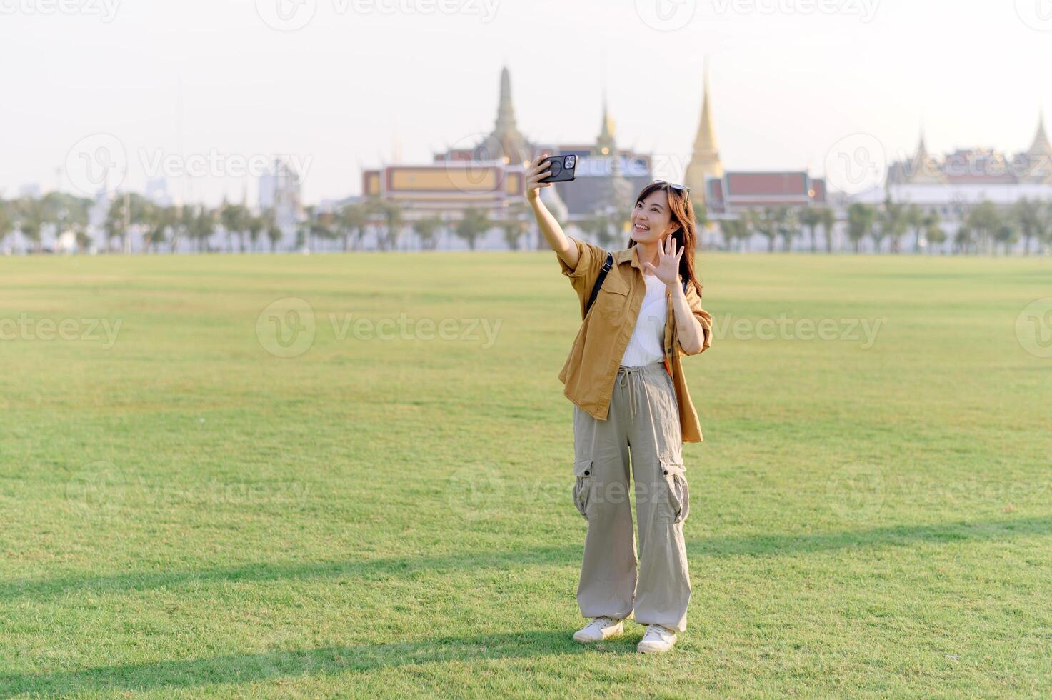 Traveler asian woman in her 30s take a livestream on smartphone while explores Wat Phra Kaew emerald Buddha. Share the wonders of Thai heritage through her journey. photo