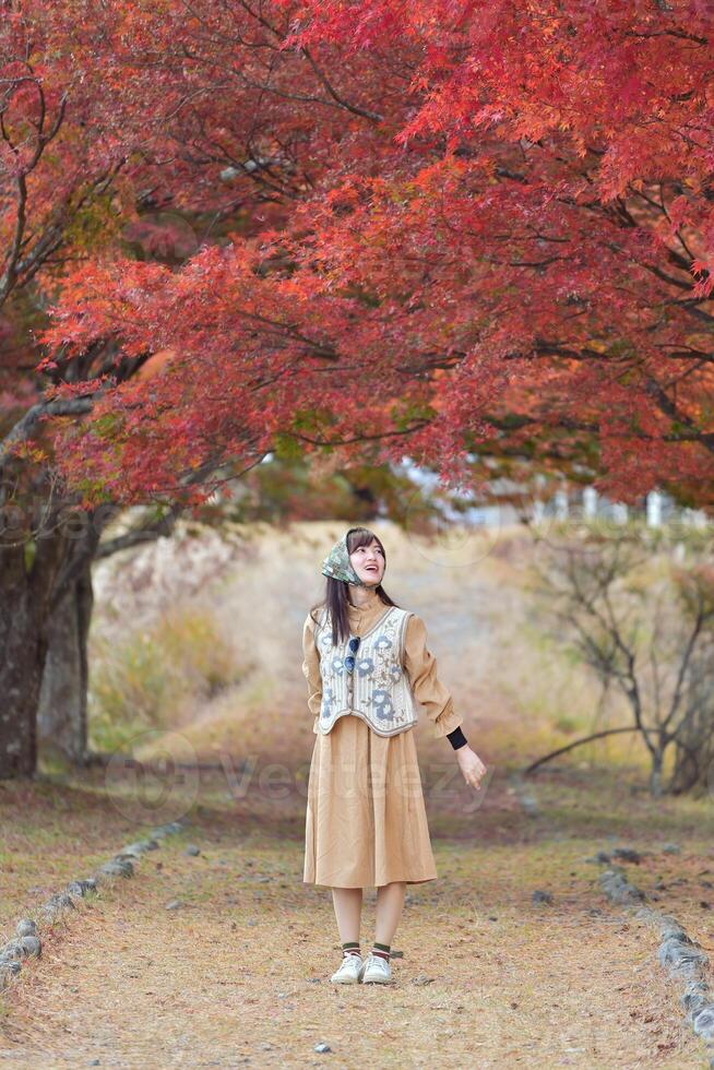 Asian woman in Japan, amidst vibrant fall foliage, smiles in a holiday portrait. Friends, selfies, and joyful moments captured by the lake near Mount Fuji. photo