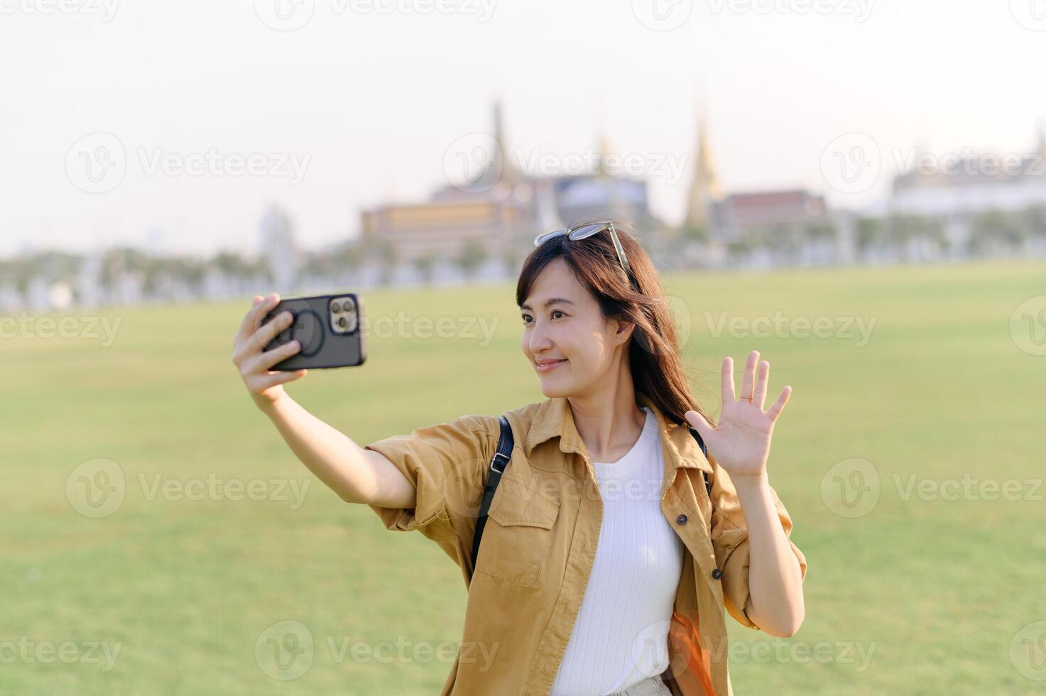 Traveler asian woman in her 30s making a livestream or selfie on smartphone while explores Wat Phra Kaew emerald Buddha. Share the wonders of Thai heritage through her journey. photo