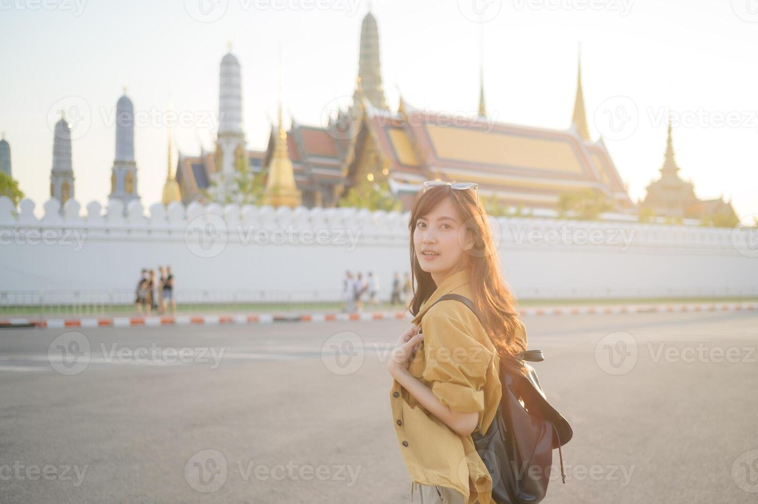 Traveler asian woman in her 30s, backpack slung over her shoulder, explores the intricate details of Wat Pra Kaew with childlike wonder. Sunlight dances on the golden rooftops. photo