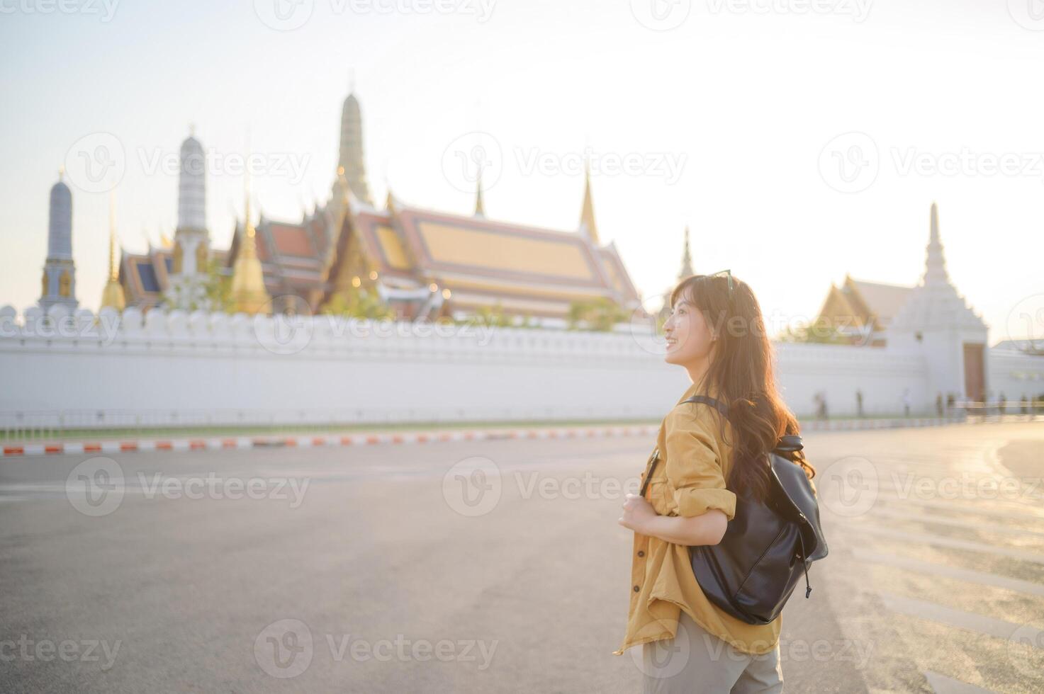 Traveler asian woman in her 30s, backpack slung over her shoulder, explores the intricate details of Wat Pra Kaew with childlike wonder. Sunlight dances on the golden rooftops. photo