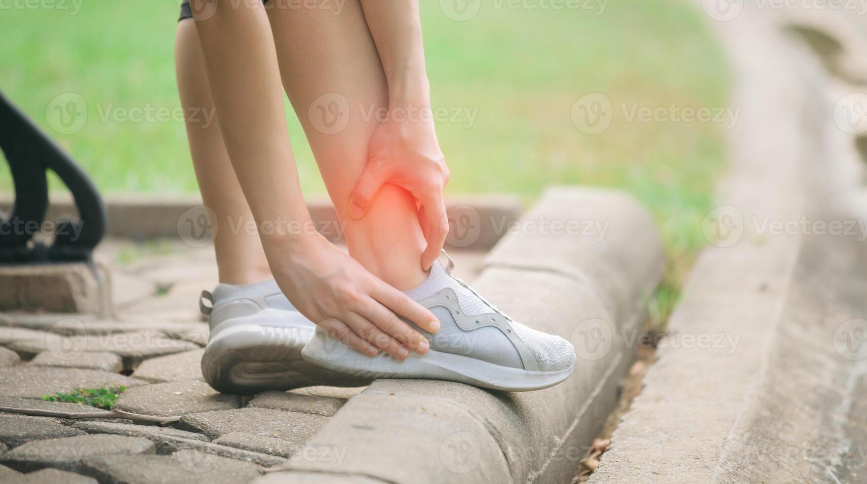 Sprained ankle problem. woman jogger. 30s asian female wearing sportswear holding her ankle with pain after running exercise in public park. photo