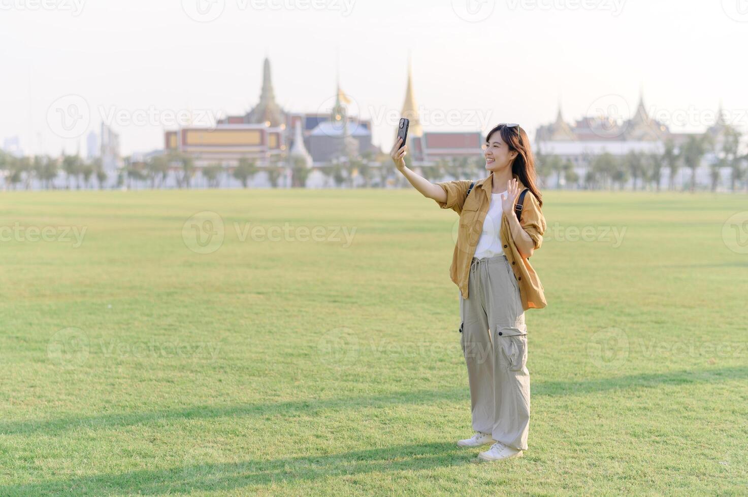 Traveler asian woman in her 30s take a livestream on smartphone while explores Wat Phra Kaew emerald Buddha. Share the wonders of Thai heritage through her journey. photo