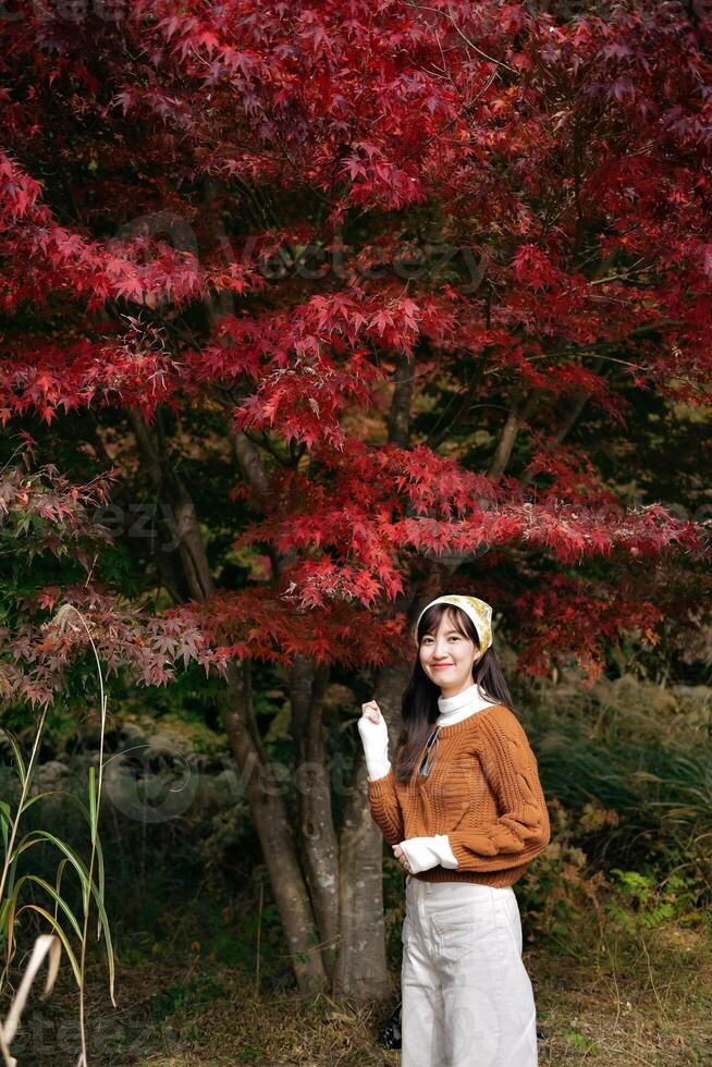 Asian woman in a fashionable sweater revels in the beauty of fall. A pretty and cheerful portrait amid nature's vibrant colors. photo