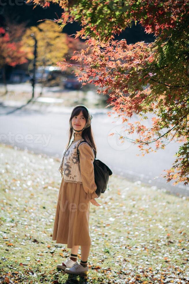 Asian woman in Kyoto's fall, wearing a casual dress, enjoys the beauty of nature, capturing cheerful smiles amid vibrant foliage and the scenic allure of Japan. photo