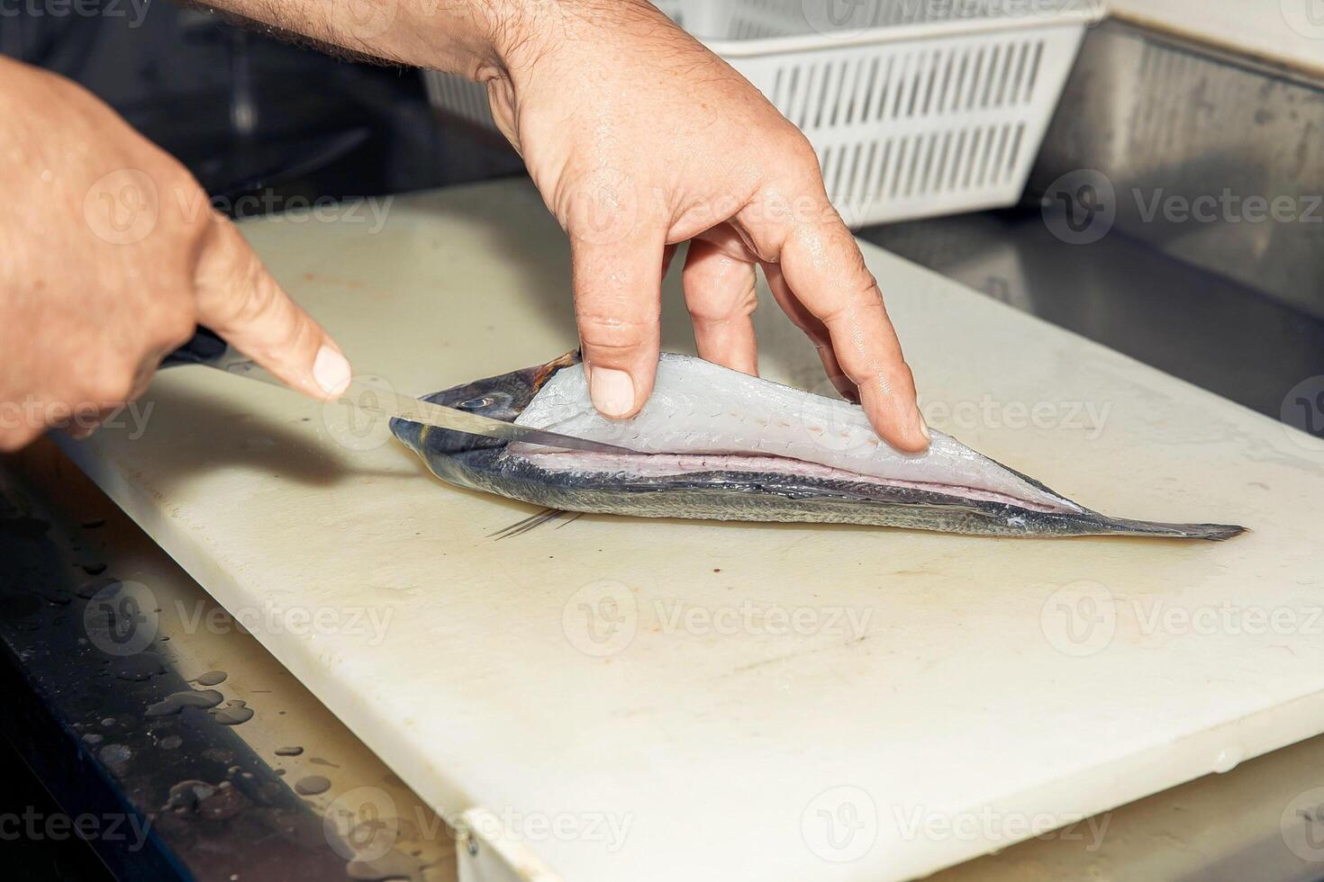 Hands carefully filleting fresh fish on cutting board in professional kitchen, fish preparation concept photo