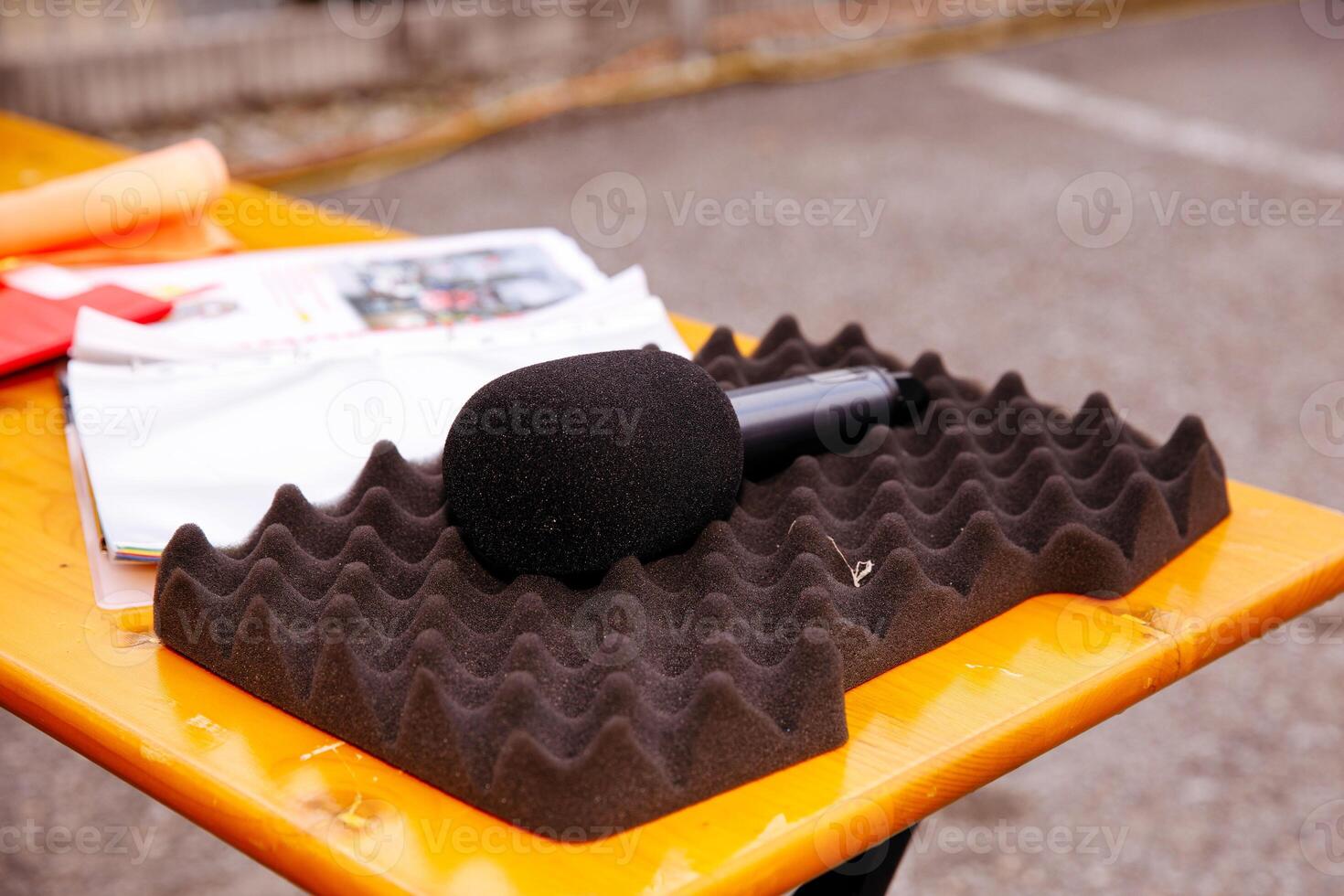 Microphone placed on soundproof foam, outdoor table setting, black and orange color contrast, interview preparation, broadcasting concept photo