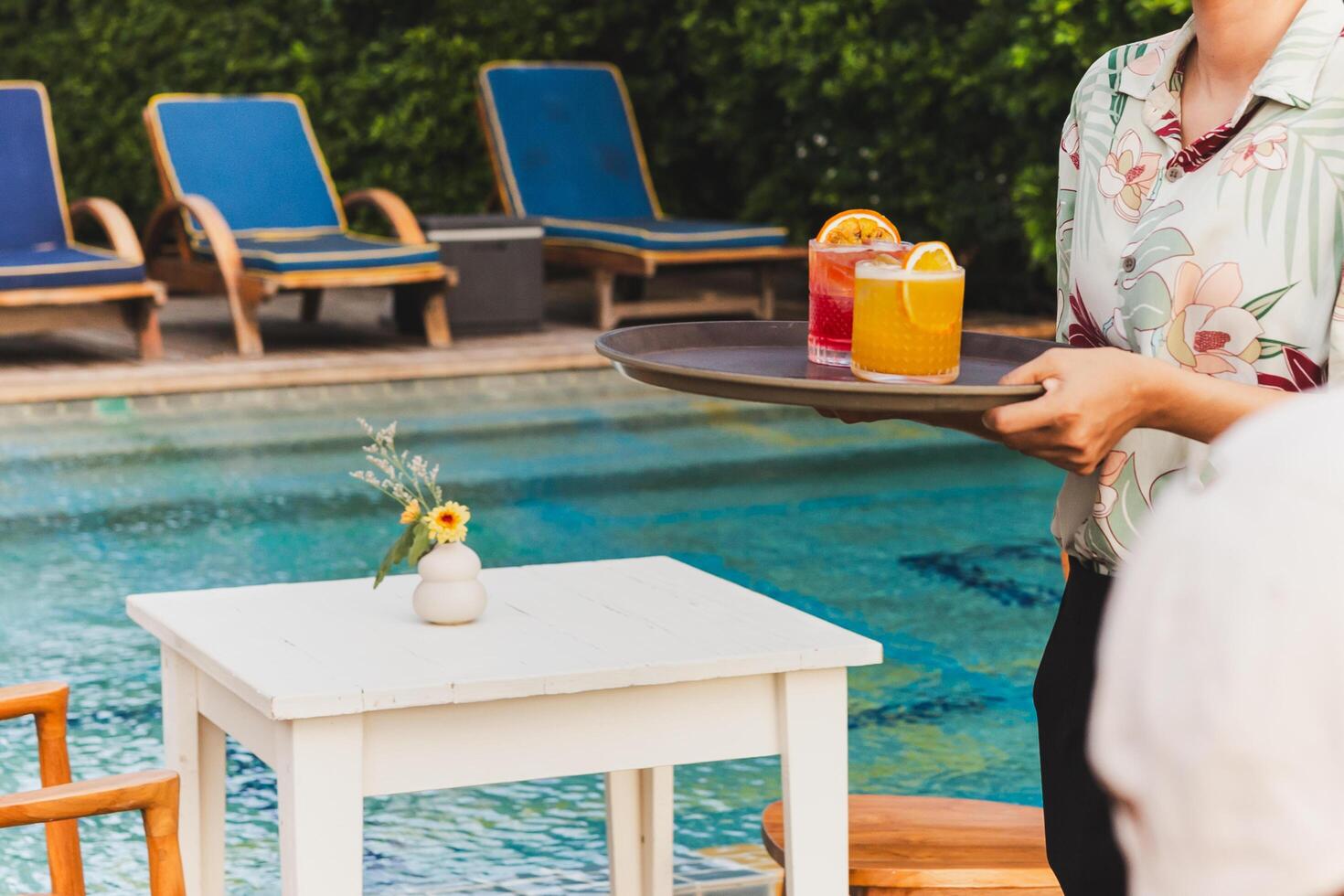 Waiter serving cocktail dink on a tray by swimming pool. photo