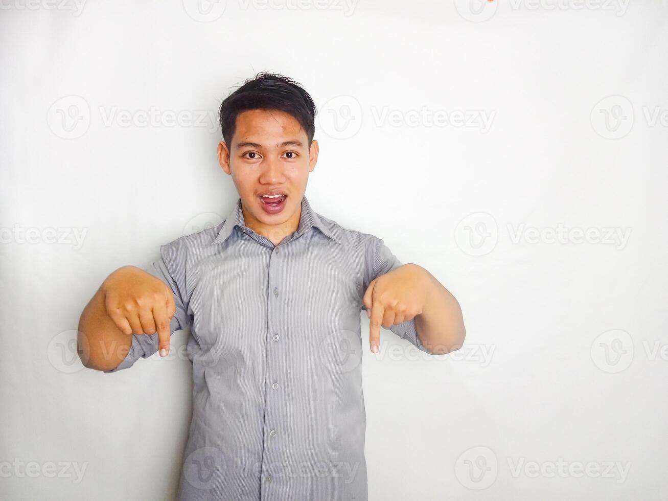 Attractive Young Asian man smiling while pointing to copy space area wearing grey shirt isolated on white background photo