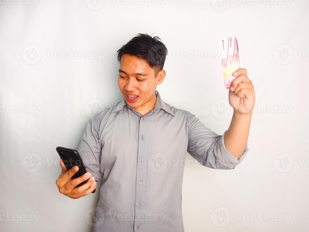 Young asian man looking to the mobile phone and money that he hold wearing grey shirt isolated on white background photo
