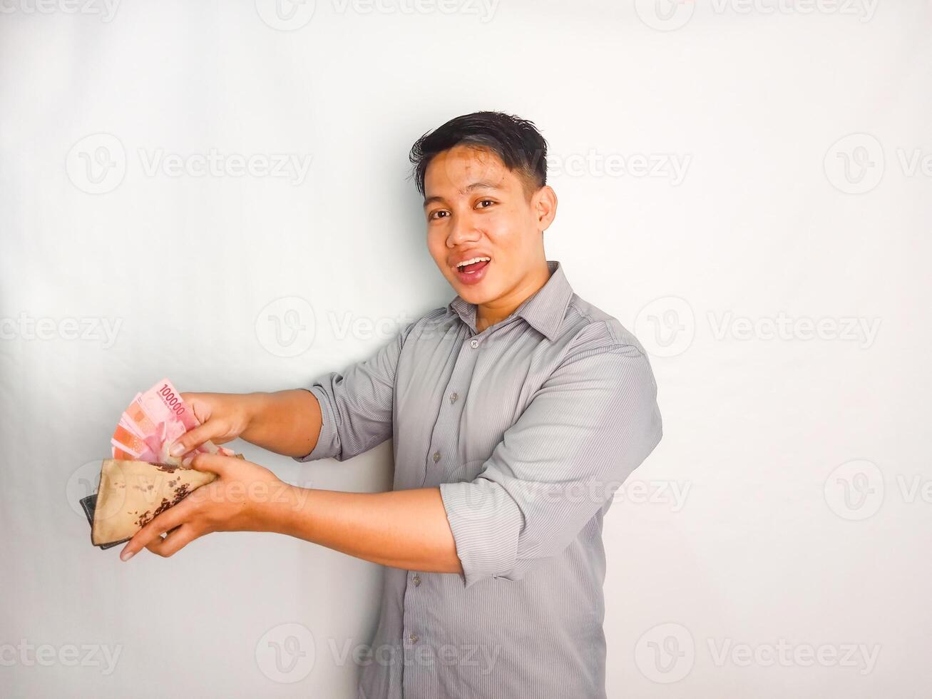 Side view of Young asian man smiling happy while taking out money from inside his wallet wearing grey shirt isolated on white background photo