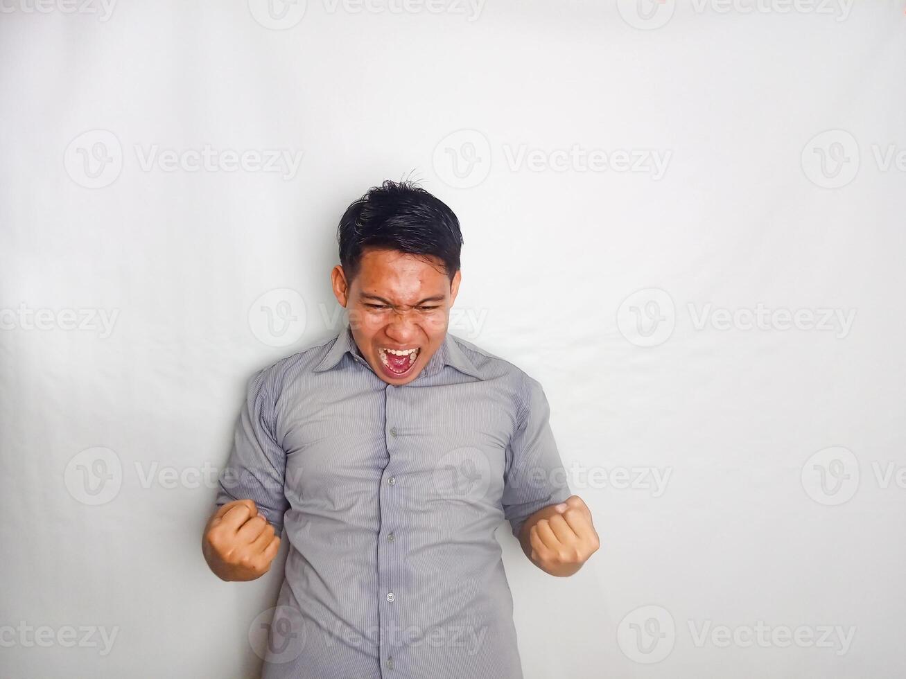 Young Asian man screaming success with his fist clenched wearing grey shirt isolated on white background photo