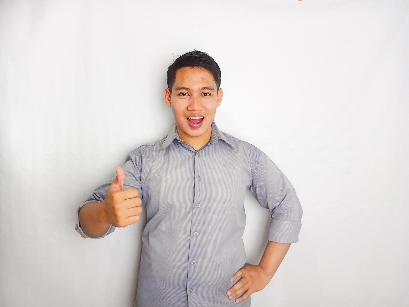 Adult Asian man smiling happy while pointing and give OK sign. wearing grey shirt isolated on white background photo