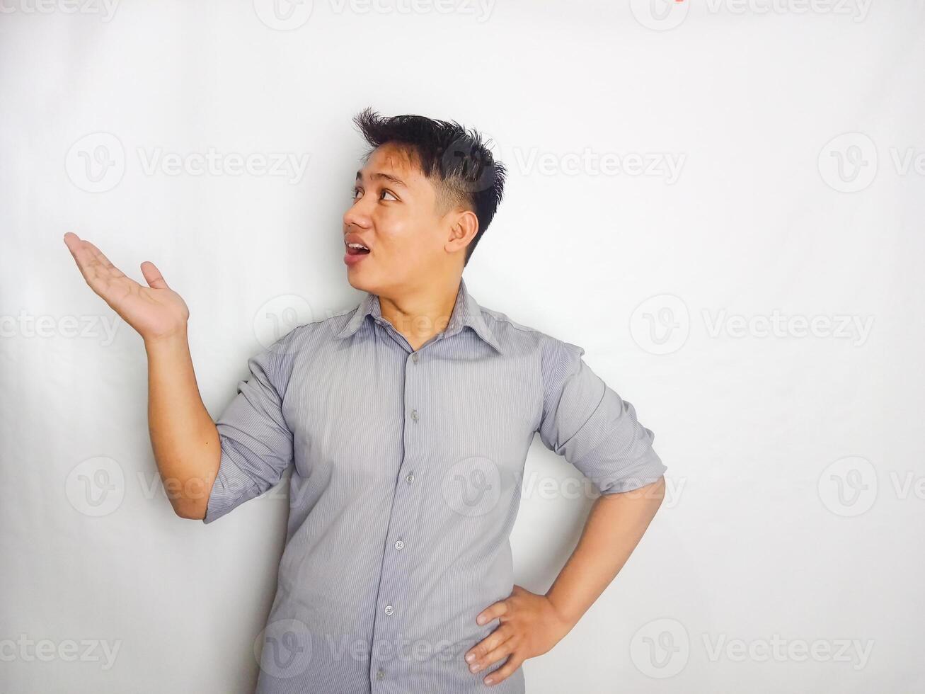 Attractive Young Asian man smiling while pointing to copy space area wearing grey shirt isolated on white background photo