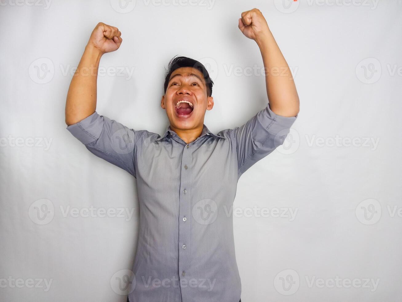 Young Asian man screaming success with his fist clenched wearing grey shirt isolated on white background photo