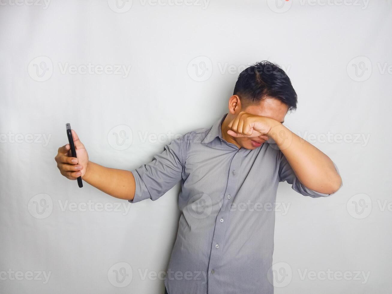 A Young man showing disappointed expression when looking to his mobile phone, wearing grey shirt isolated on white background photo