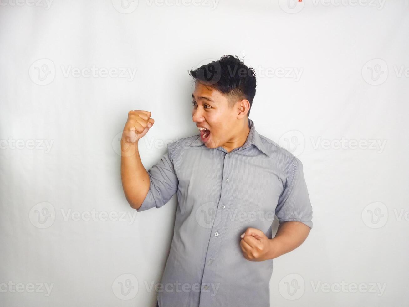Young Asian man screaming success with his fist clenched wearing grey shirt isolated on white background photo