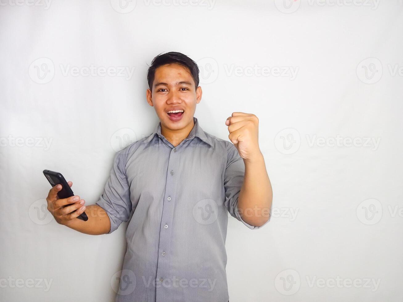 Young Asian man showing wow face expression when looking to his mobile phone wearing grey shirt isolated on white background photo