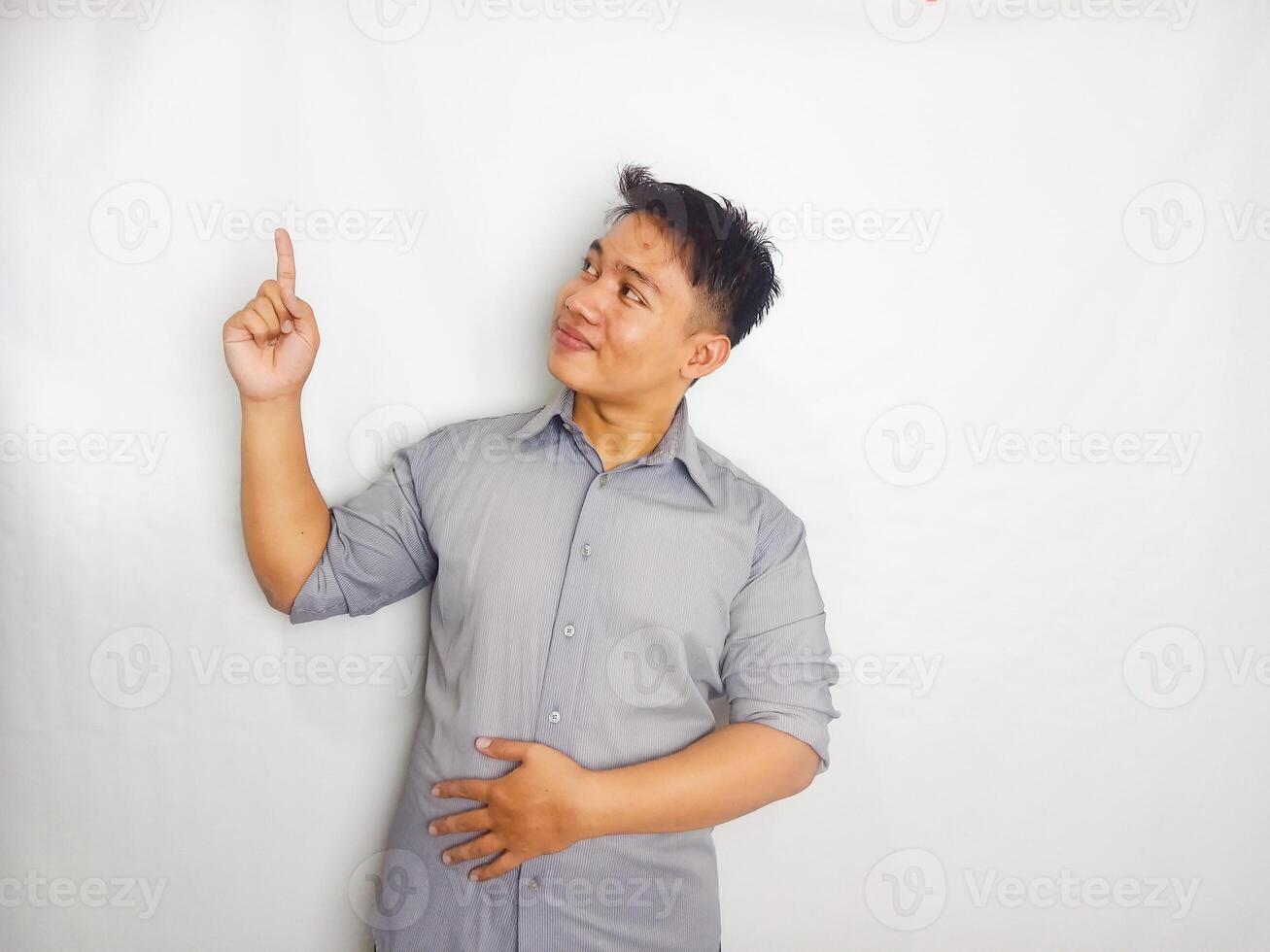 Attractive Young Asian man smiling while pointing to copy space area wearing grey shirt isolated on white background photo