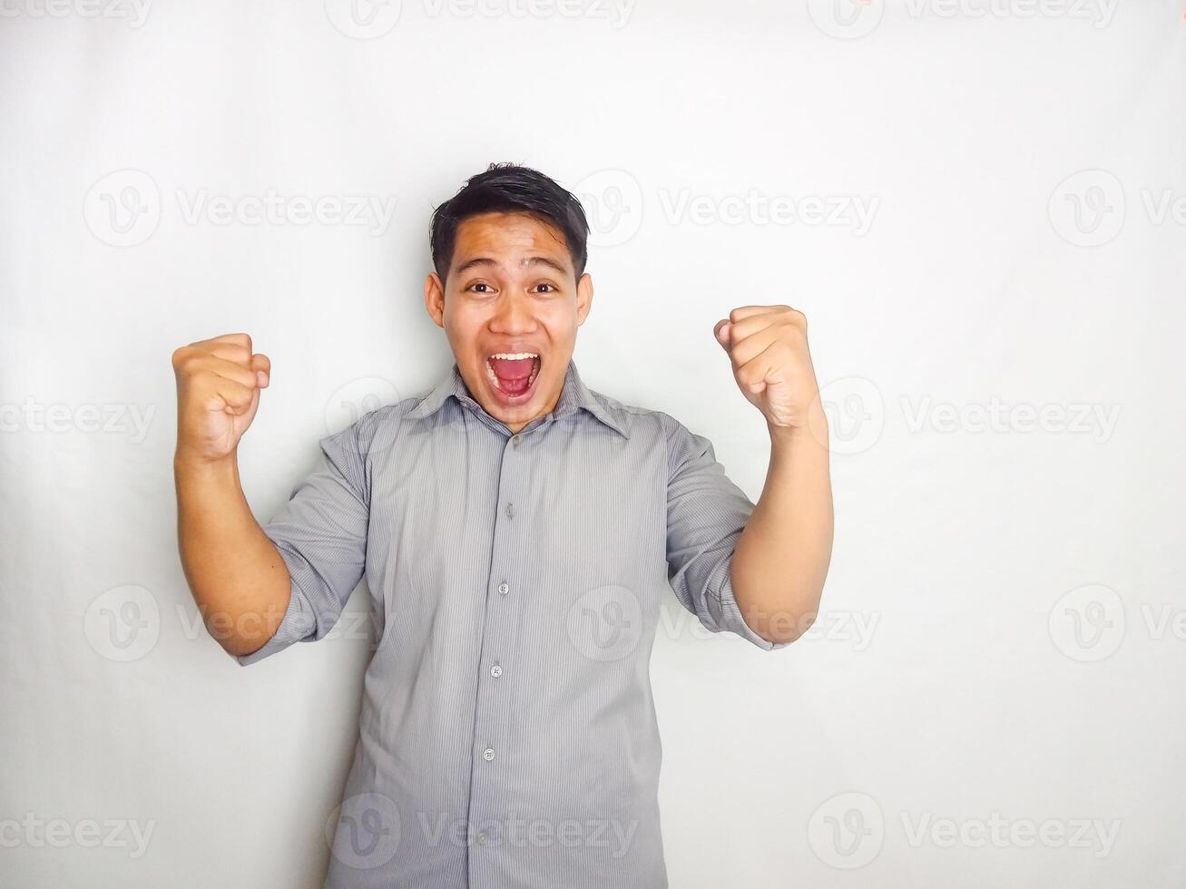 Young Asian man screaming success with his fist clenched wearing grey shirt isolated on white background photo
