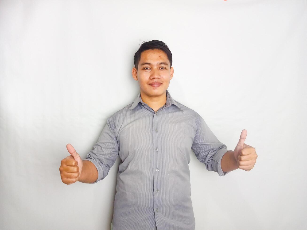 Adult Asian man smiling happy while pointing and give OK sign. wearing grey shirt isolated on white background photo