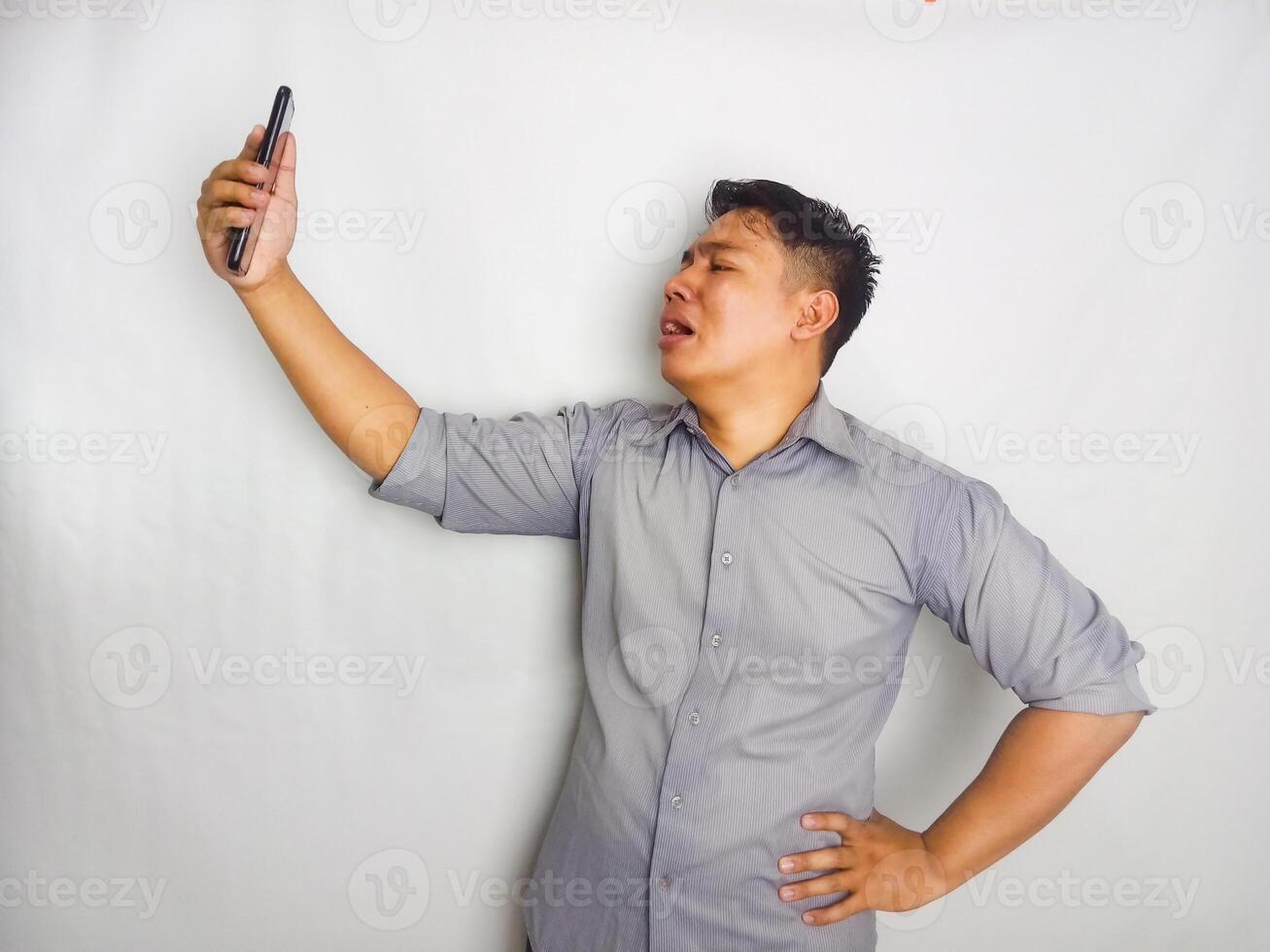 A Young man showing disappointed expression when looking to his mobile phone, wearing grey shirt isolated on white background photo